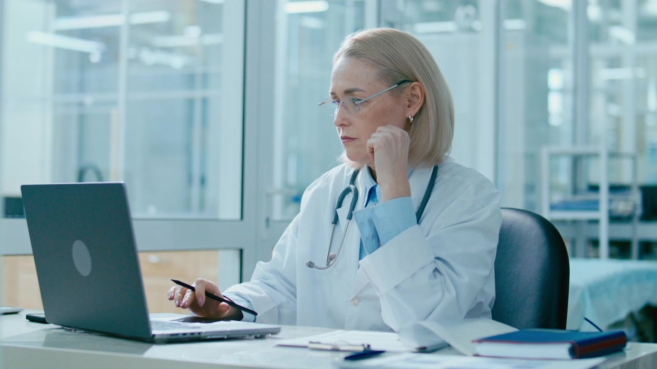 Kvindelig læge arbejder på bærbar computer og skriver journaler på klinik