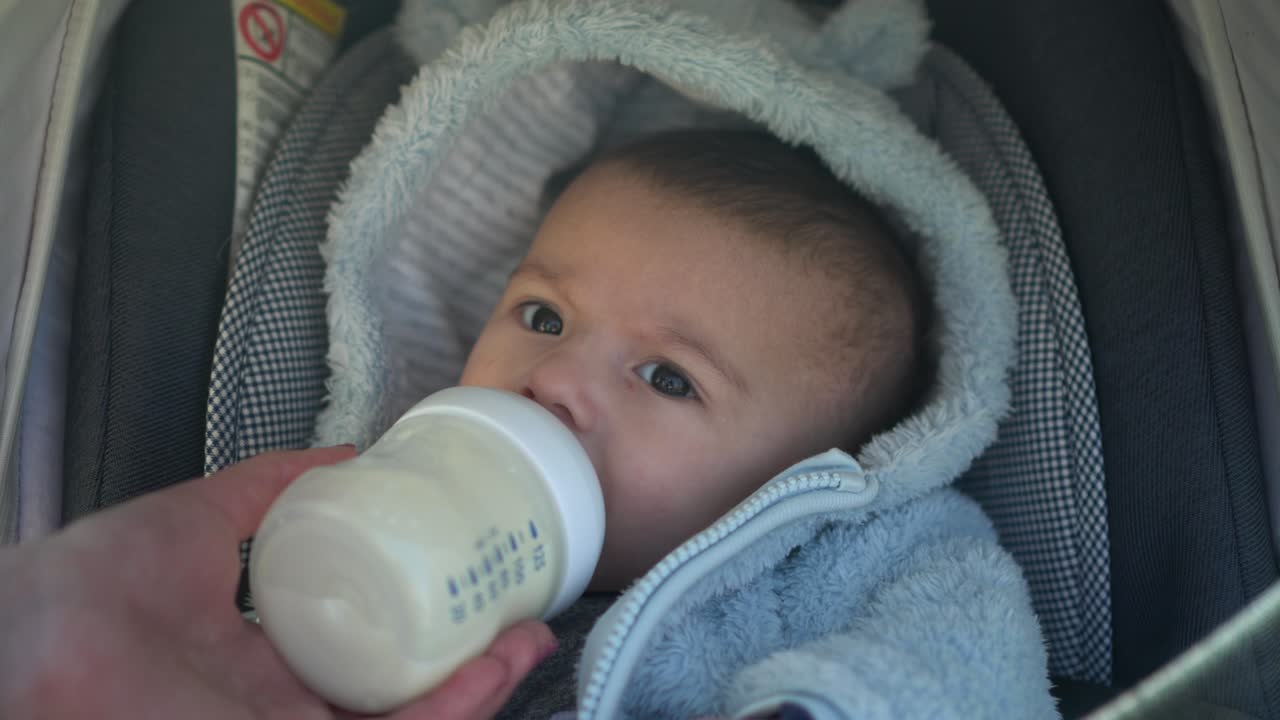 Un bambino in passeggino succhia il latte dal biberon. Un neonato mangia durante una passeggiata, primo piano.