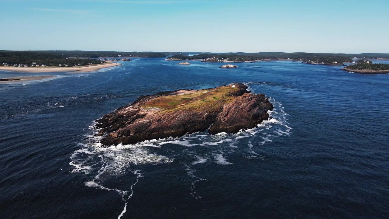 Ripresa circolare con drone intorno allo storico faro di Pond Island su una piccola isola vicino a Popham Beach, Maine, con gabbiani in volo e onde che si infrangono sull'isola rocciosa alla foce del fiume Kennebec