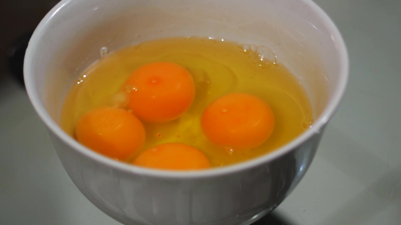 Nærbilde av rå egg i hvit bolle med sakte zoom inn, konsept for matlaging