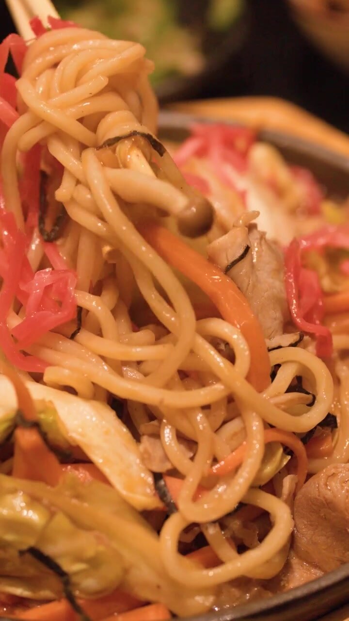 Bacchette di legno sollevano noodles yakisoba saltati in padella da una piastra in ghisa sfrigolante