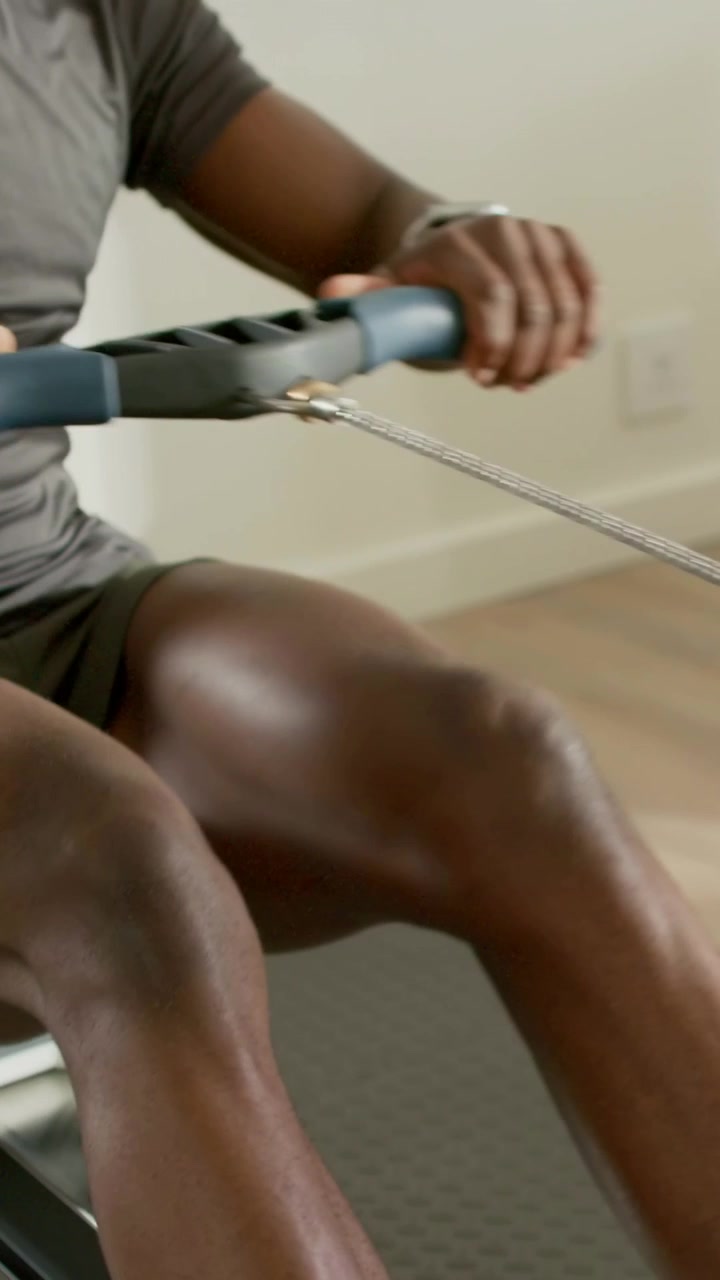 Vertical video: Gripping handle, man in gray shirt doing rowing strokes in home gym for strength