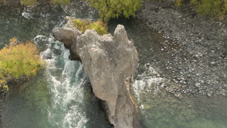 breathtaking aerial shot circling a large rock formation in the white rapids of a river in argentina