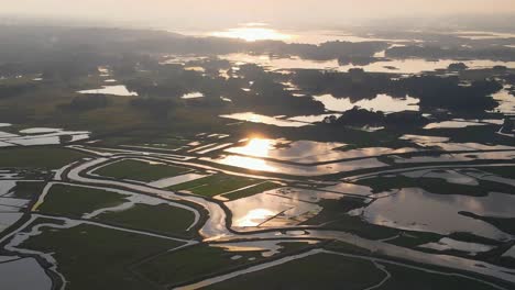 sunrise sunlit flooded agricultural farmland across sylhet, bangladesh, aerial view above glowing wetland