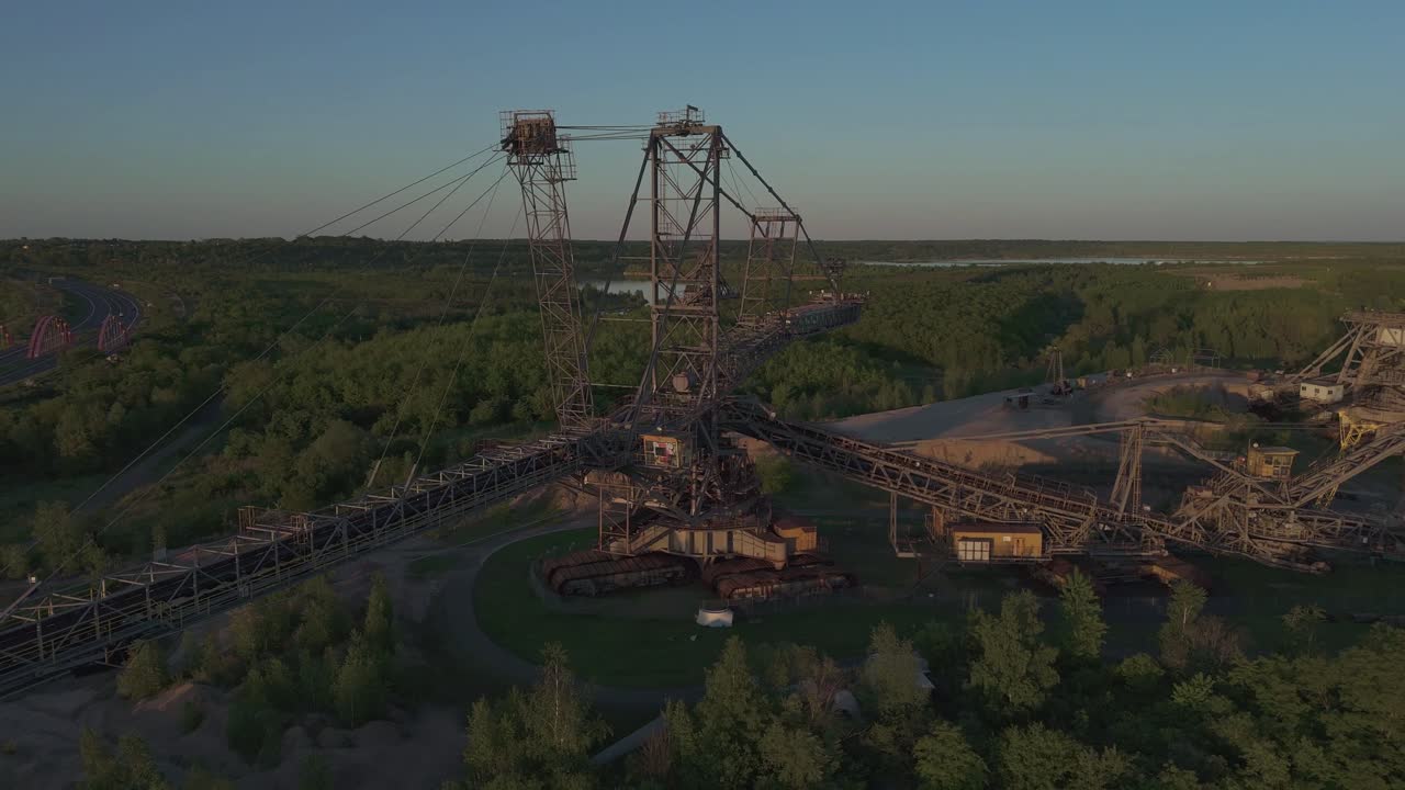 Aerial reveal of a colossal lignite stacker in Leipzig’s former mining area. Surrounded by forests and lakes, the structure is bathed in warm sunset light – a striking symbol of industrial heritage.
