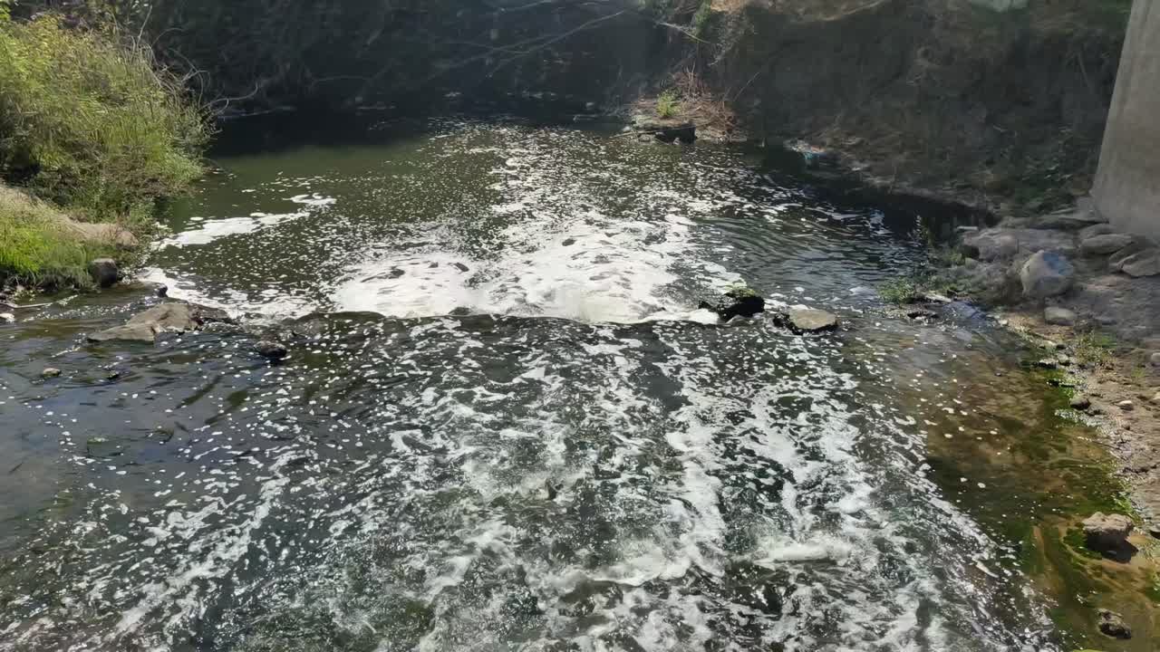 Closeup of fast-moving shallow river water cascading over rocks in forest. Natural stream, bubbles, foam, spring sunlight. Ideal 4K nature background for meditation, travel and documentaries.