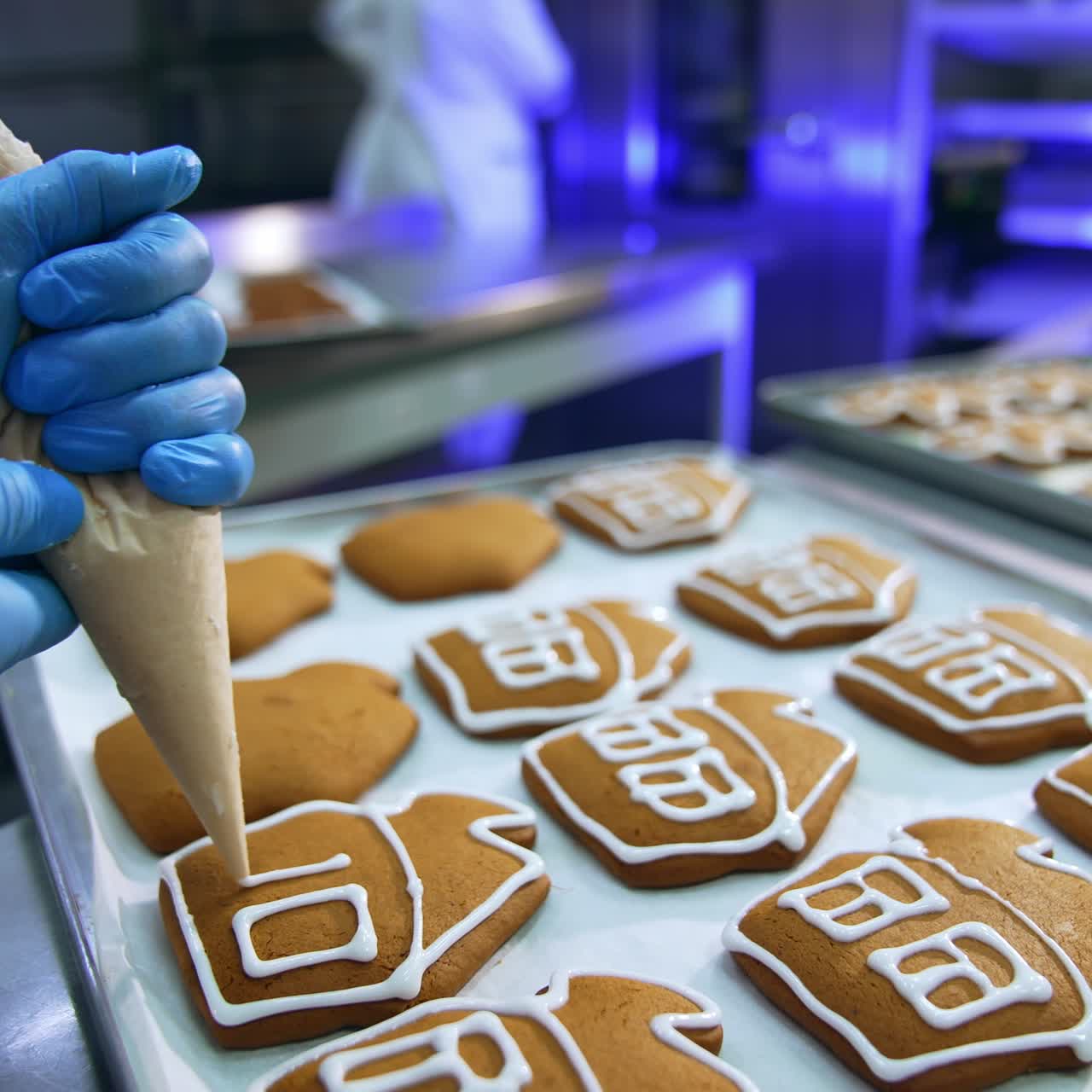 Brown freshly-baked gingerbread houses decoration. Confectioner uses pastry bag to put white cream onto the cookies. Close up
