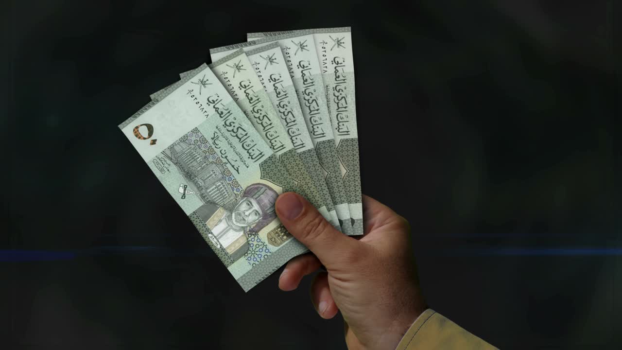 Ventaglio di banconote del Rial dell'Oman in mano.