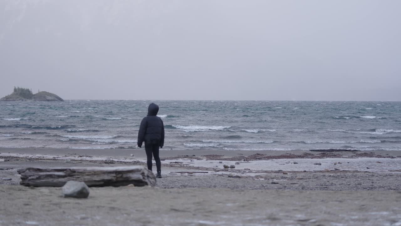 Reflective travel scene with person alone on beach, wrapped in winter clothing, Bariloche, Argentina
