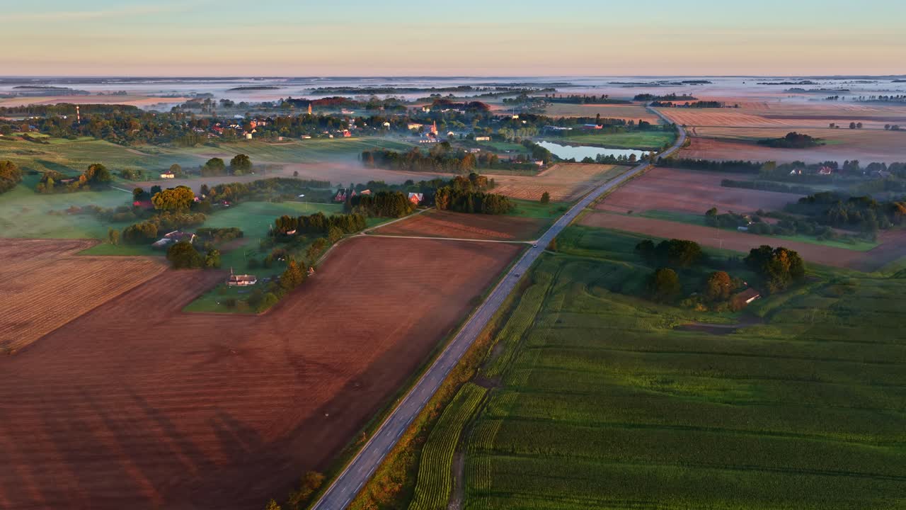 Sweeping drone of patchwork farmland, roads and fields in golden early morning light, mist fog on ground