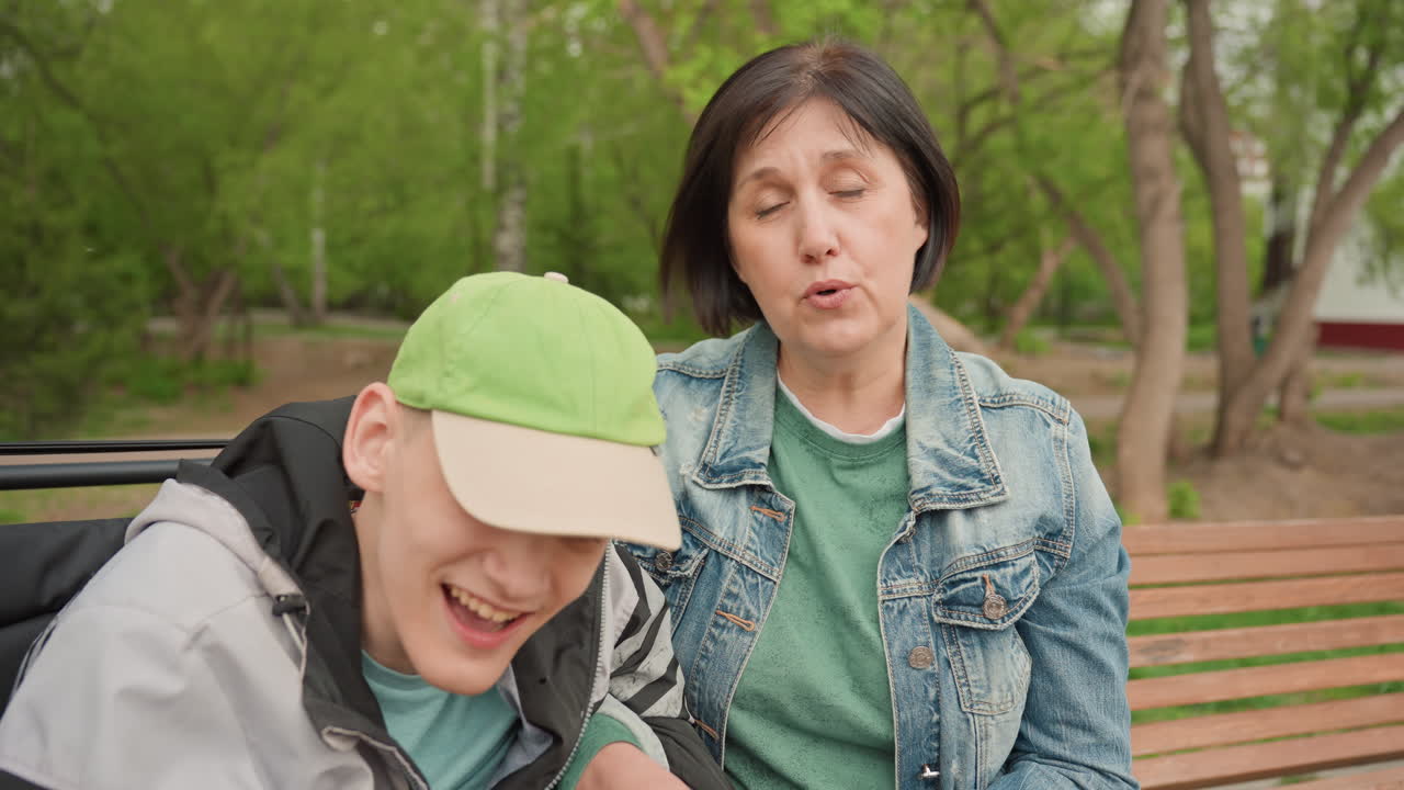 Young Man In Wheelchair And Caregiver Sit In Quiet Reflective Conversation On Bench, Woman Listens With Thoughtful Expression While Man Leans Forward, Calm Park Scenery And Soft Light Create