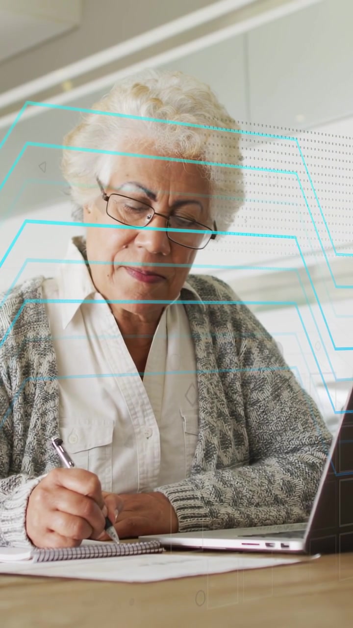 Vertical video: Pan showing senior woman noting on PC as cyan overlay sweeping over desk for tech