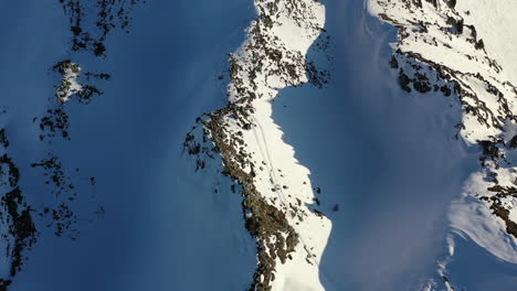 Drone-shot,-dolly-forward-while-looking-down-on-to-snow-covered-valley-ridges-filled-with-shadows-and-contours,-in-La-Plagne-France