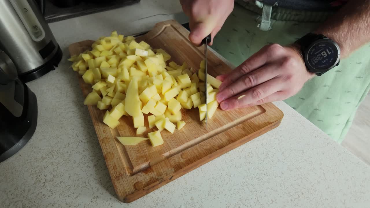 Plano estático a cámara lenta de un hombre cortando patatas en cubos sobre una tabla de cocina