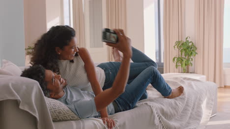 happy couple taking photo together using camera having fun relaxing at home on sofa enjoying romantic relationship