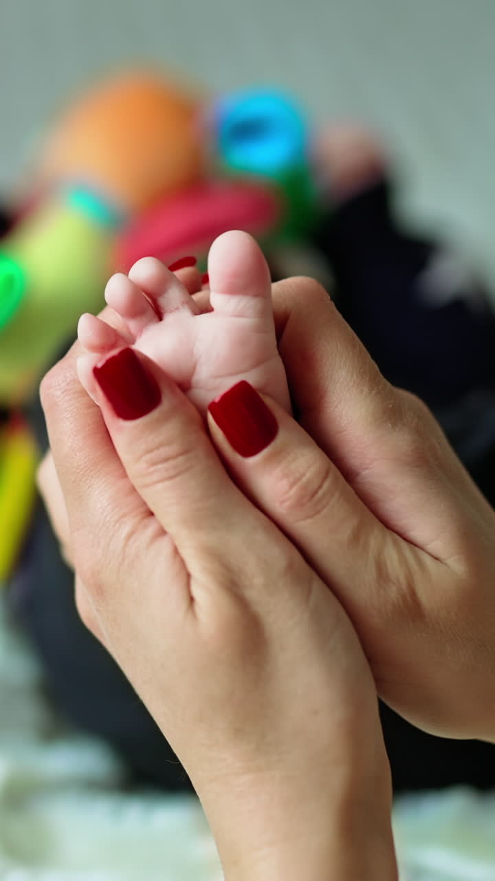 Mother massaging her baby's tiny foot with her thumbs. Little kid trying to take his legs away. Close up. Blurred backdrop. Vertical video