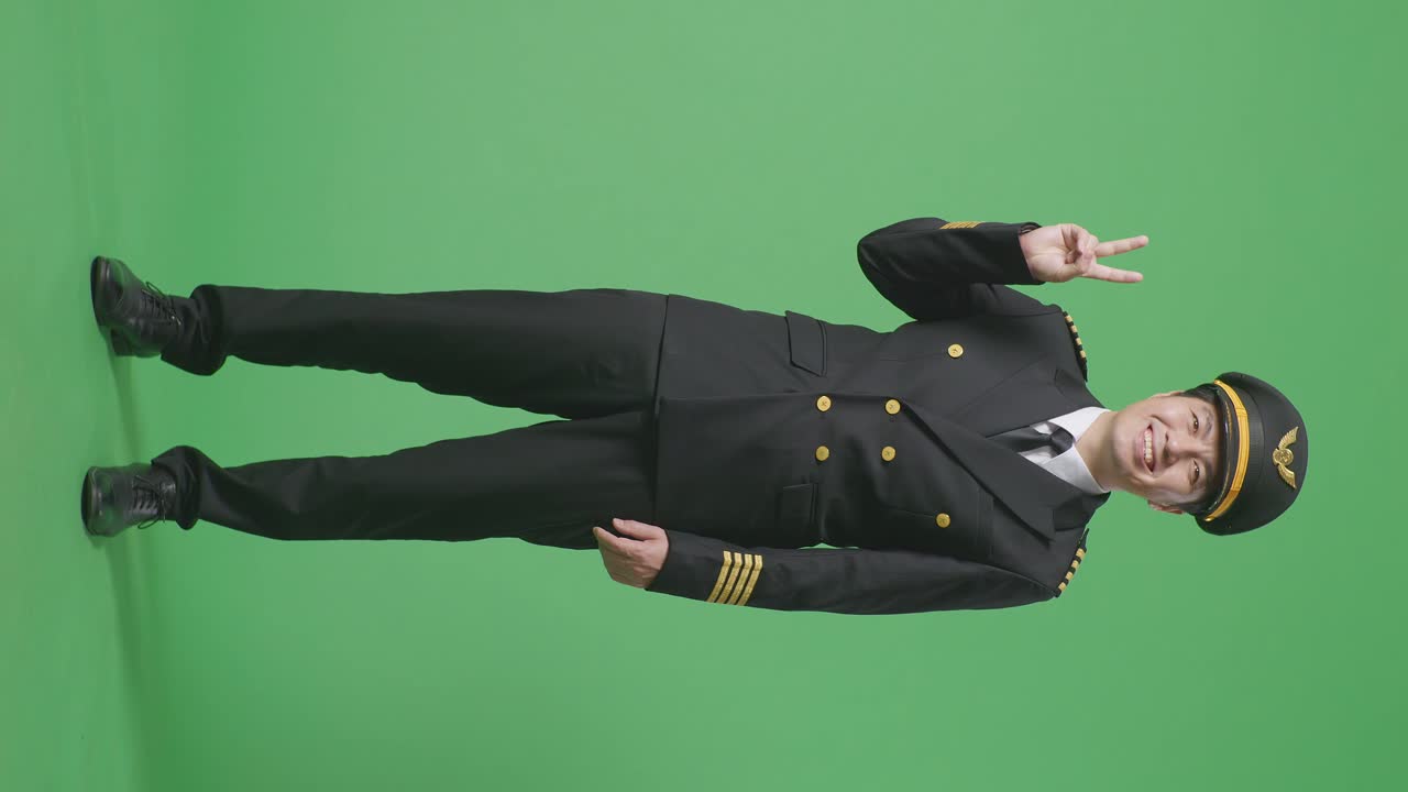 полное тело азиатского мужчины пилот улыбается и показывает мир жест к камере в то время как стоит в зеленом экране фоновой студии