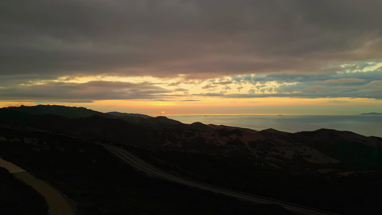 toma panorámica aérea de un gran molino de viento que trabaja en un terreno montañoso al atardecer