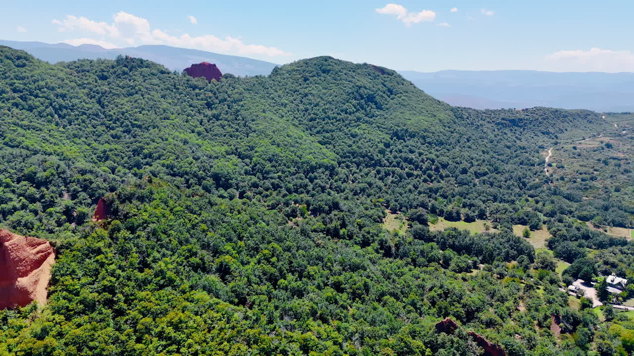 Mountains covered with thick lush greenery on sunny day. Some private houses located in the valley at the rock foot. Aerial view.