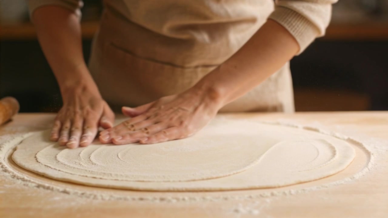 Le mani di un fornaio con un grembiule beige che modellano l'impasto da cuocere su un bancone da cucina con un mattarello