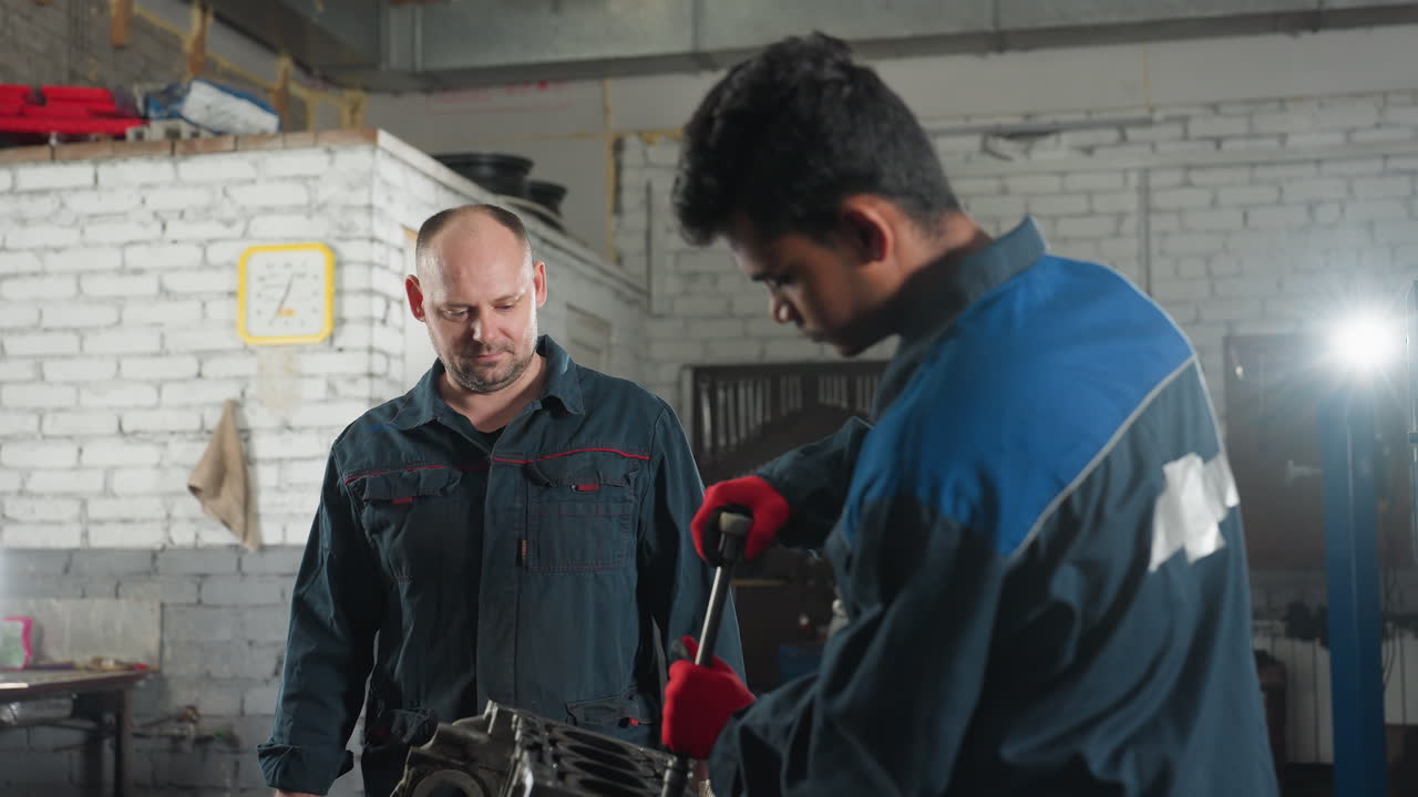 mecánico en el taller trabajando en el motor del coche, apretando la nuez con guantes rojos mientras el colega observa, el fondo presenta herramientas de trabajo, reloj de pared amarillo y luz brillante que ilumina el espacio de trabajo