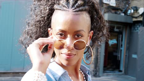 joven negra de moda con vestido azul girando y mirando a la cámara sobre sus gafas de sol, de cerca