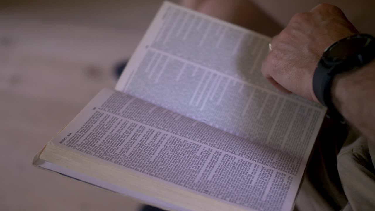 Un uomo che legge e sfoglia le pagine della sua Bibbia nel libro di Giosuè all'interno di un'antica chiesa.