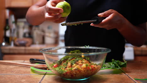 small particles of a lime peel tumble into a bowl of ingredients for a healthy homemade meal - slow motion