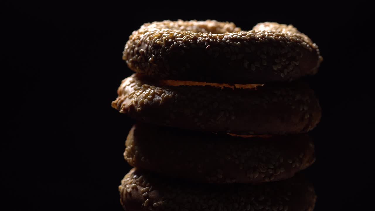 Bagel freschi con semi di sesamo in rotazione. Sfondo nero. Primo piano estremo