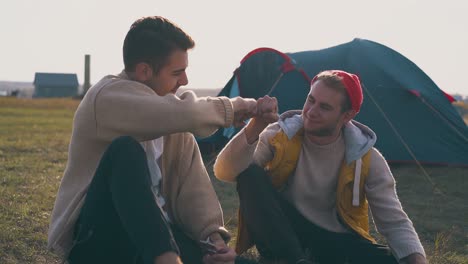 smiling men talk resting at blue tent in camp on meadow