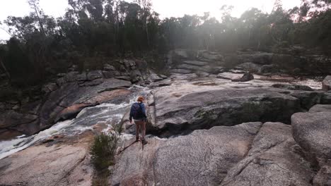 un hombre caminando sobre una cascada cerca de un desfiladero rocoso en la selva australiana