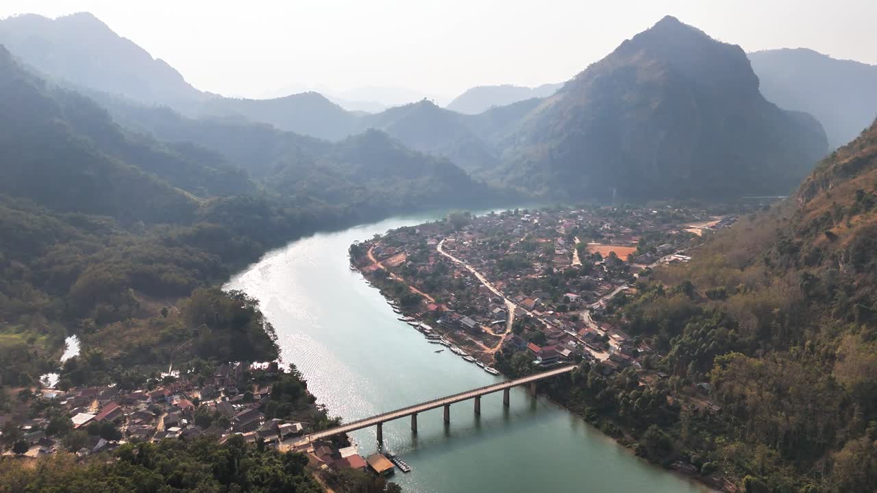 Aerial view of Nong Khiaw showing the Nam Ou River crossed by the Nong Khiaw Bridge, with the village nestled between forested limestone mountains in northern Laos