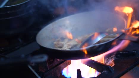 stirring meat pieces in pan on gas stove with bright orange flames