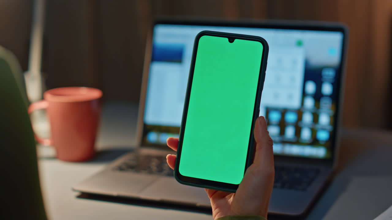 Girl hand holding chromakey cellphone working late at home office close up.