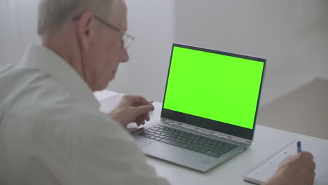 una persona de edad avanzada está aprendiendo en línea utilizando una pantalla verde de portátil para la tecnología de llave de croma educación a distancia