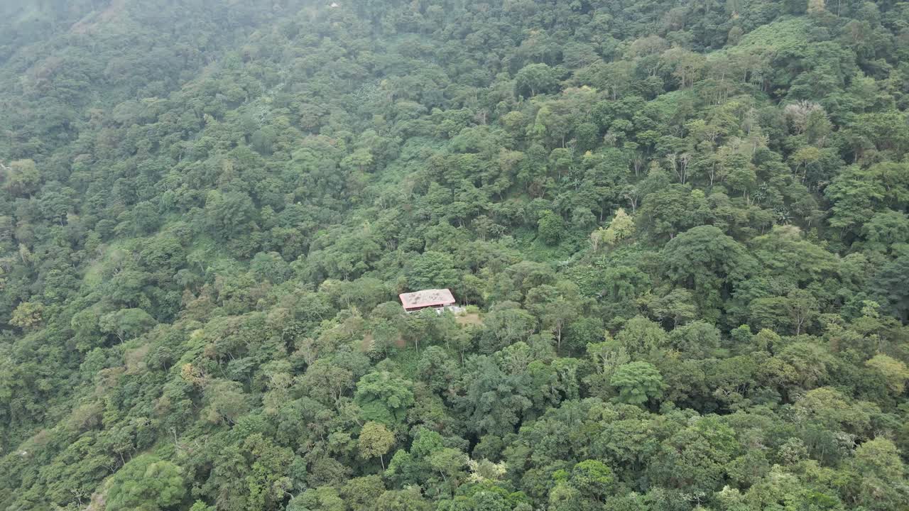 el dron lentamente se desplaza y gira en círculos sobre una casa solitaria rodeada por los densos pisos boscosos de las montañas de la sierra nevada en colombia.