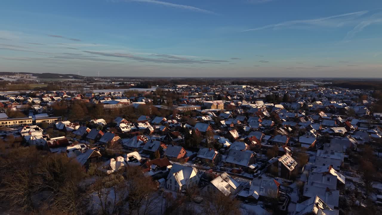 Tysk boligkvarter ved solnedgang. Sneklædte hustage og tæt bebyggelse lyser op i det varme aftenlys og afslører et roligt forstadsmiljø under en klar himmel. Luftoptagelse. Bredt billede
