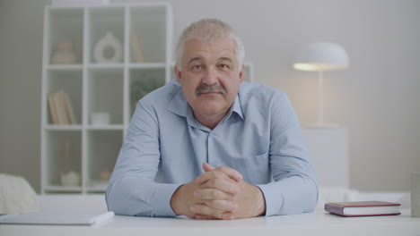 adult man is listening and nodding head looking at camera sitting at table in room medium portrait shot