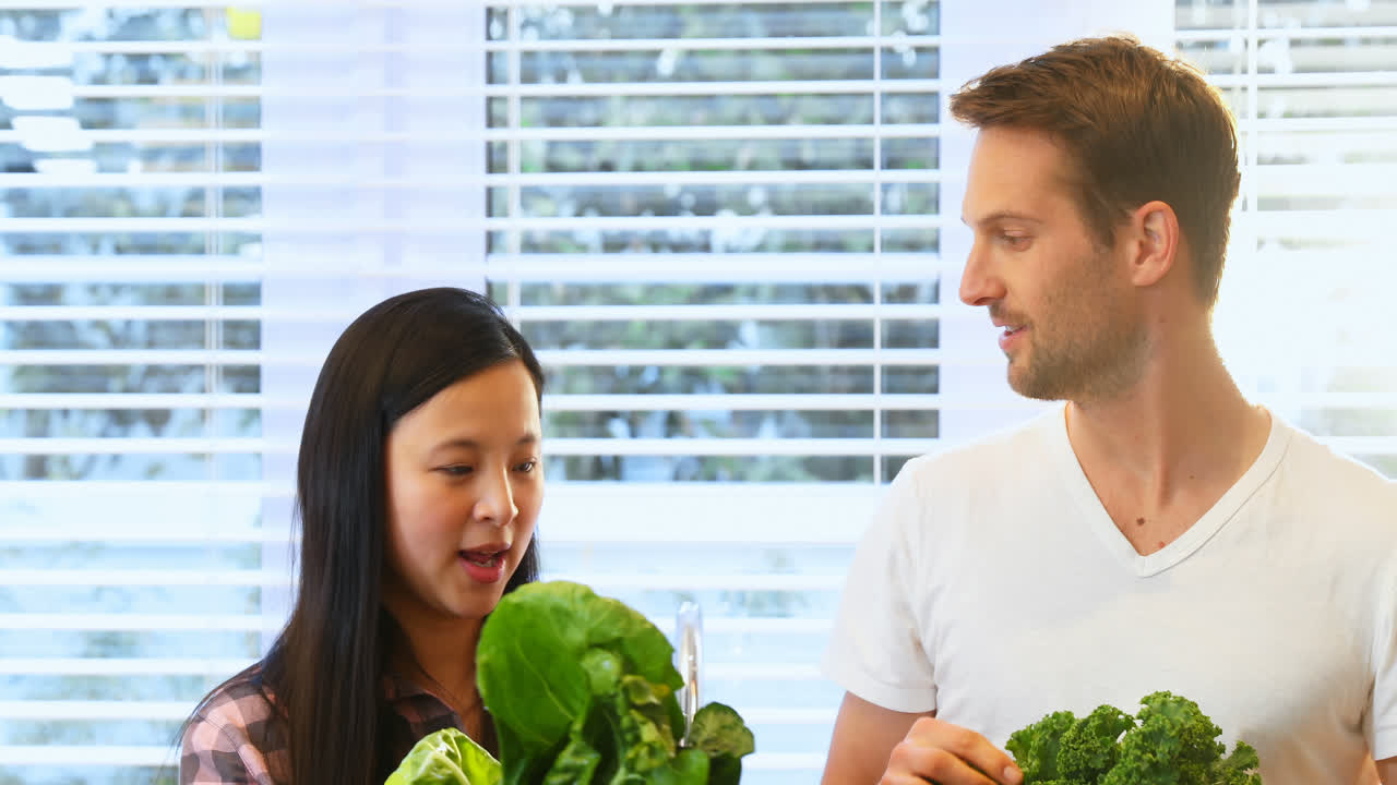 임신 한 부부 가 주방 4k 에서 신선 한 잎 채소 를 들고 있다