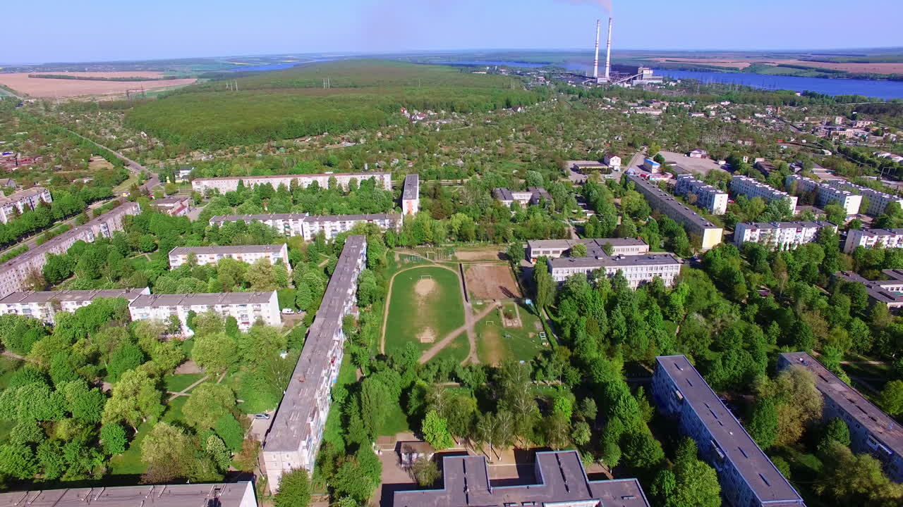 Big green city panorama on summer day. Drone footage over the residential area at the backdrop of blue river, farmlands and woods.