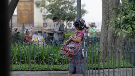 antigua guatemala woman wears traditional colorful handmade dress, walking on main town square with various souvenirs for sale, wearing face mask due to recent covid-19 pandemic - slow motion