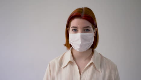 Woman-shaking-head-like-saying-no,-showing-thumb-down-as-a-sign-of-denial-or-disapproval,-wearing-medical-face-mask-with-gloves.-Copy-space-and-white-background.