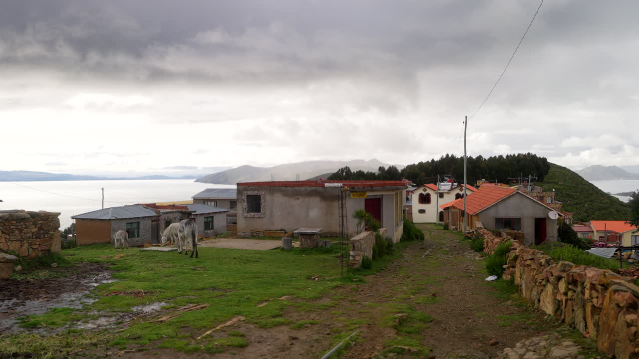 Peaceful rural scene on Bolivia’s Isla del Sol overlooking Lake Titicaca, showing grazing donkeys, stone walls and traditional buildings under soft cloudy light