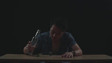 drunk asian man crying and pouring vodka in a shot glass before drinking in black background