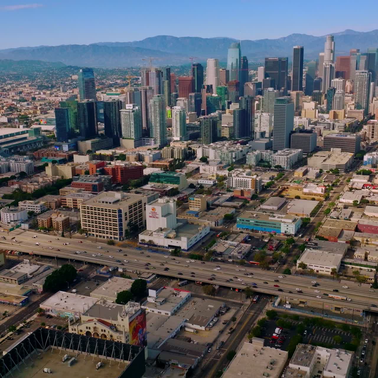 Famous skyscrapers standing among the low buildings of Los Angeles, California, USA. Numerous cars moving by the freeway at daytime. Aerial view