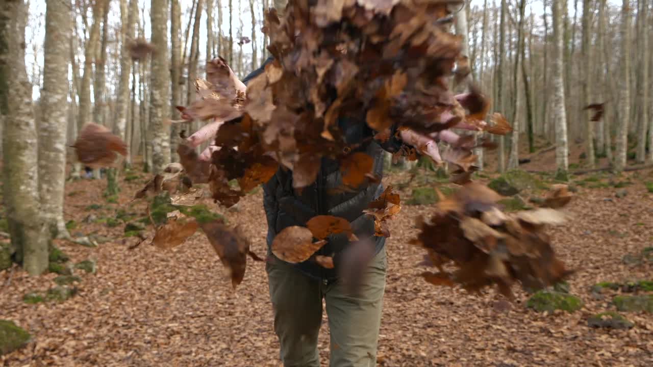 el hombre sonriente sonríe arroja hojas secas hacia la cámara en el bosque