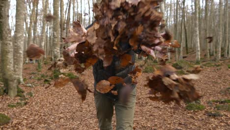 Smiling-man-smiles-throws-dry-leaves-towards-camera-in-woods
