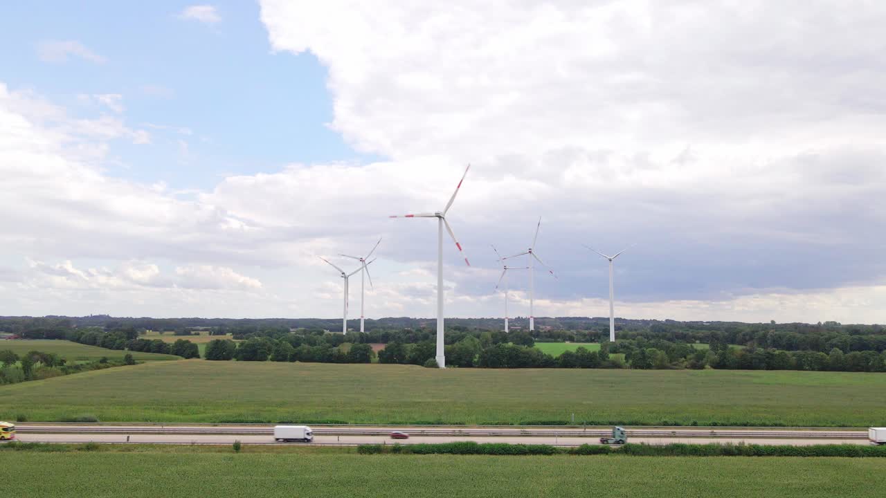 Drone footage of wind turbines beside a highway, surrounded by farmland and cornfields