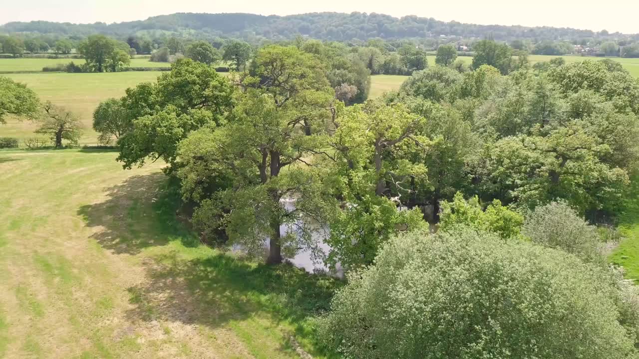 Drone flying over agricultural farmland in Cheshire, UK near Alderley Edge and showing natural pond