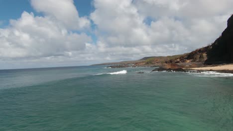 Disparo-De-Un-Dron-Fpv-Moviéndose-Hacia-Atrás-Alrededor-De-Una-Pequeña-Isla-Rocosa-Y-Sobre-Una-Playa-En-El-Soleado-Hawaii